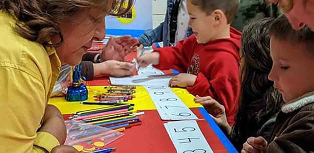 Background: Kids in school using crayons and colored pencils while learning numbers - Caption: None 